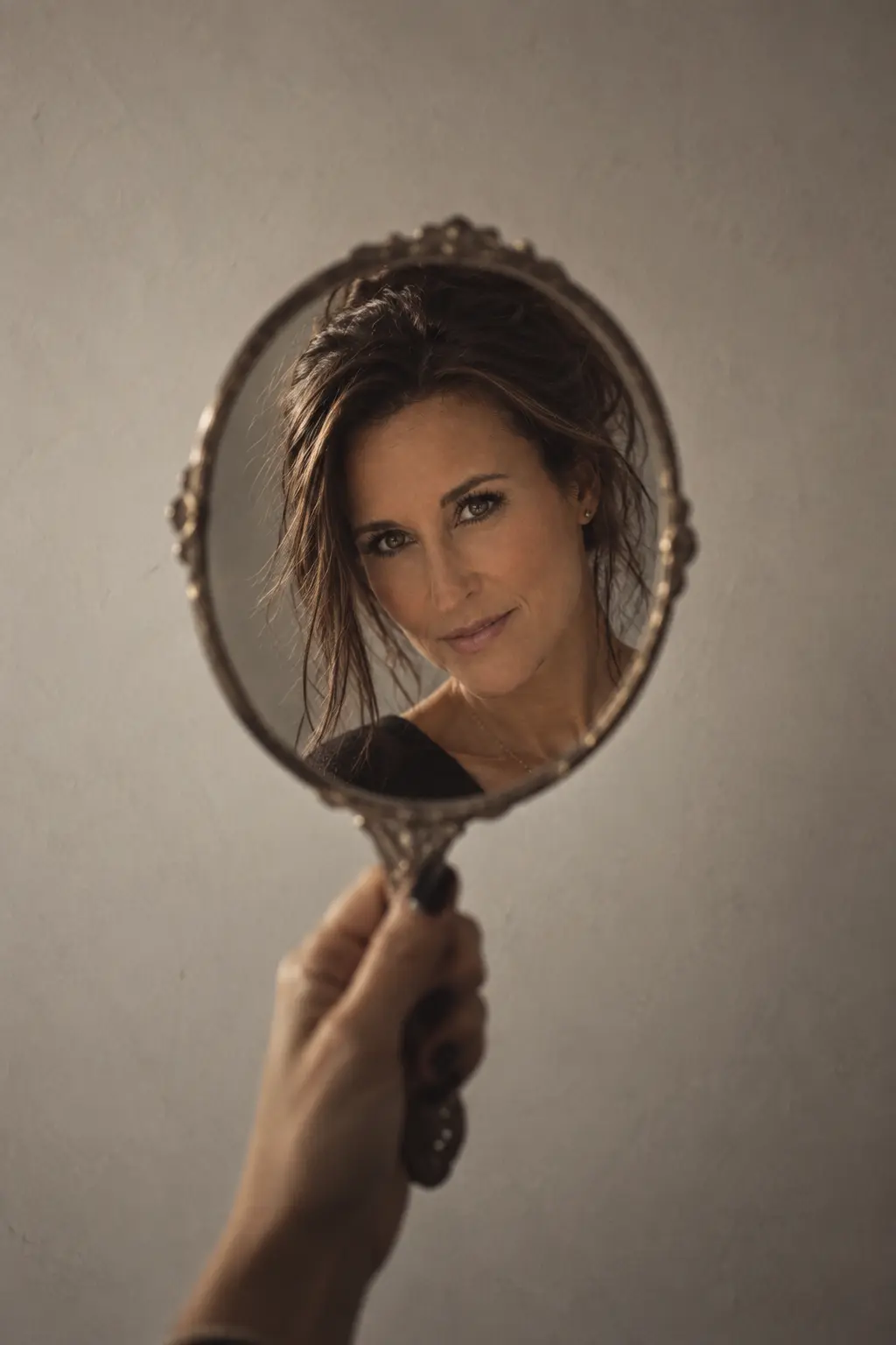 Lore Lassen reflected in an antique handheld mirror held against a pale wall